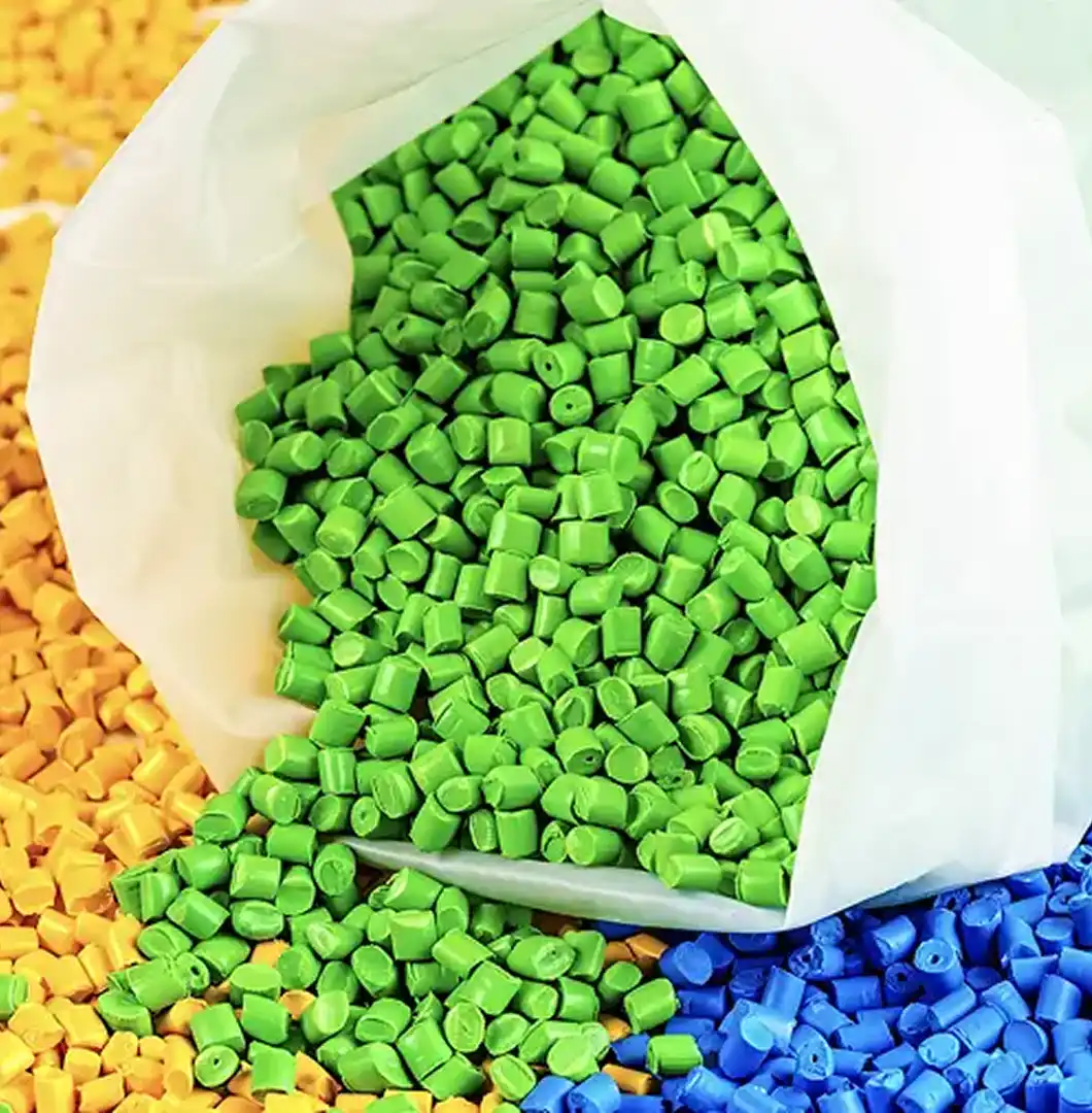 A close-up shot of an open white bag filled with bright green polypropylene compound pellets, surrounded by scattered yellow and blue granules.