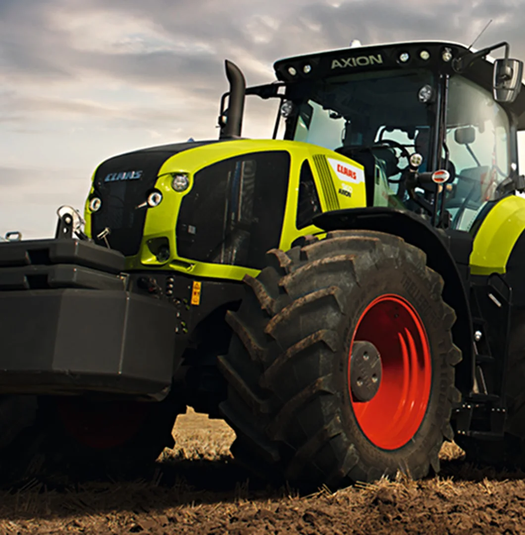 A close-up shot of a large, modern green and black CLAAS Axion agricultural tractor parked in a field under a cloudy sky.