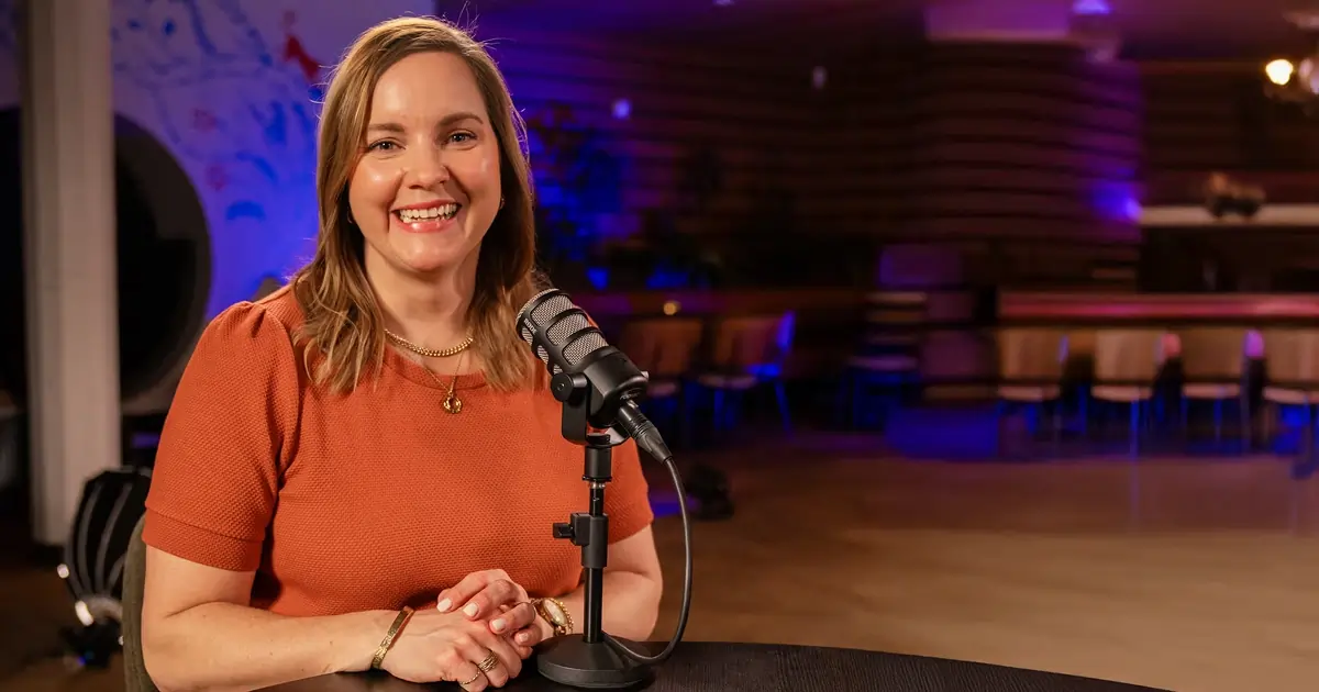 Anne Koopman in front of a podcast mic in a orange shirt