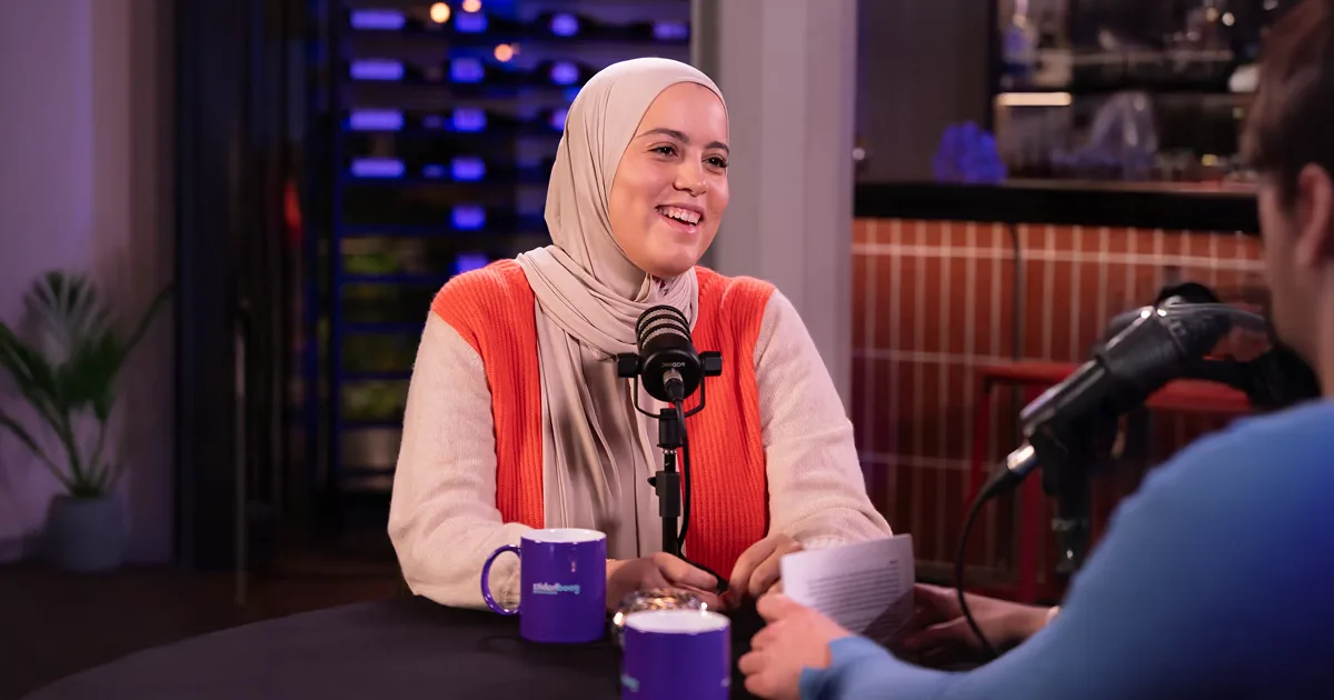 Hanan Challouki, communication expert and author, sat in front of mic wearing a beige hijab and orange sweater.
