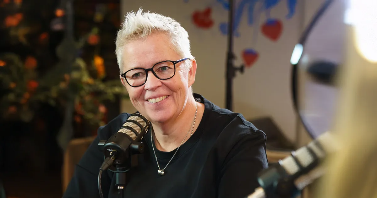 Jeanne Bakker sitting in front of mic wearing with a black tshirt with black glasses and short hair
