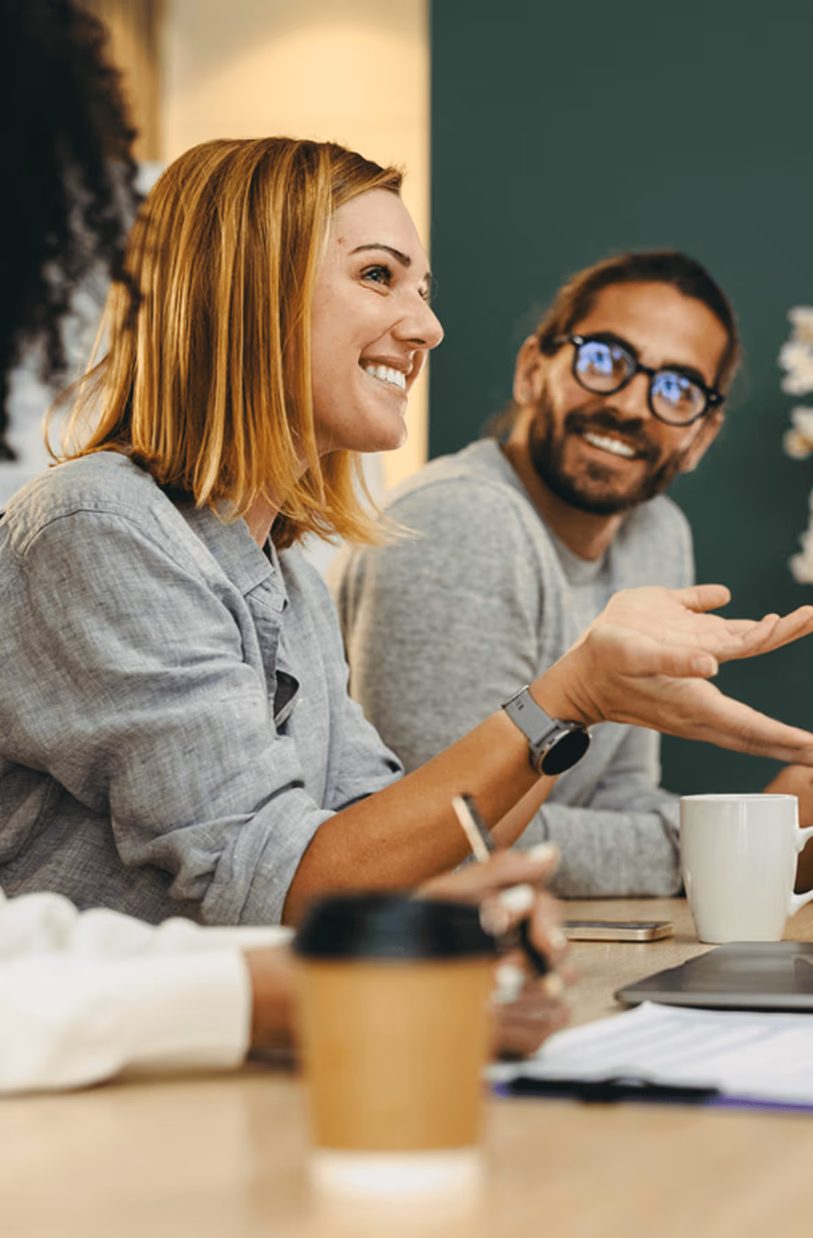 Lächelnde Frau und Mann bei Besprechung, entspannte Atmosphäre, Kaffebecher, Notizen.