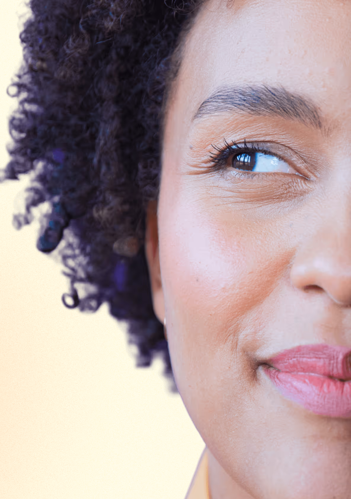 Frau mit lockigem Haar vor gelbem Hintergrund, lächelt dezent.