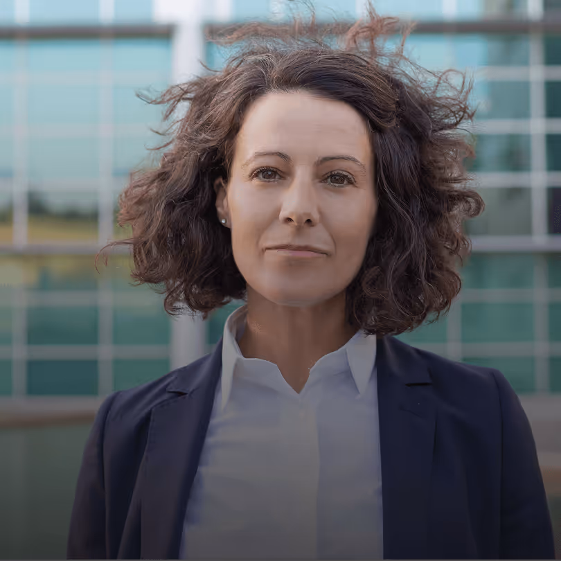 Professionelle Frau mit lockigem Haar in Business-Kleidung vor modernen Glasgebäuden.
