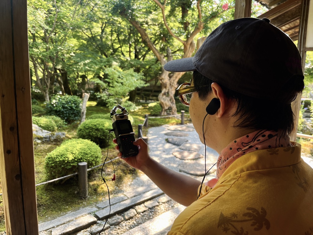 A photograph of a recent sound walk guest who joined a Kyoto, in Sound walk. This photograph is of the sound of a Kyoto Garden being captured with a sound recorder by a young man wearing binaural microphones in his ears.