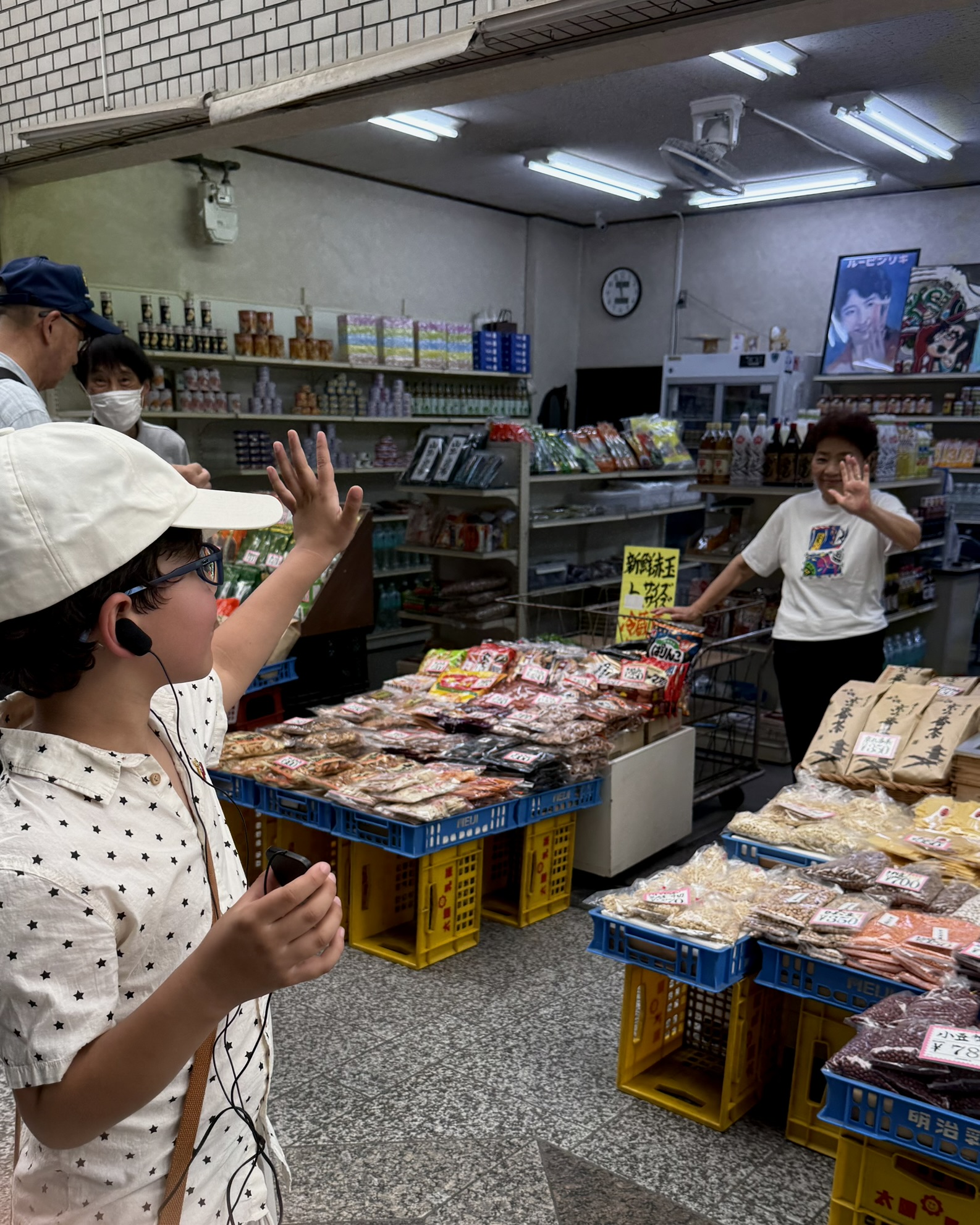 A photograph of a recent sound walk guest who joined a Kyoto, in Sound walk. The photograph features a young boy waving at a Japanese lady whilst he records sound in Demachiyanagi Shopping Street in Kyoto.