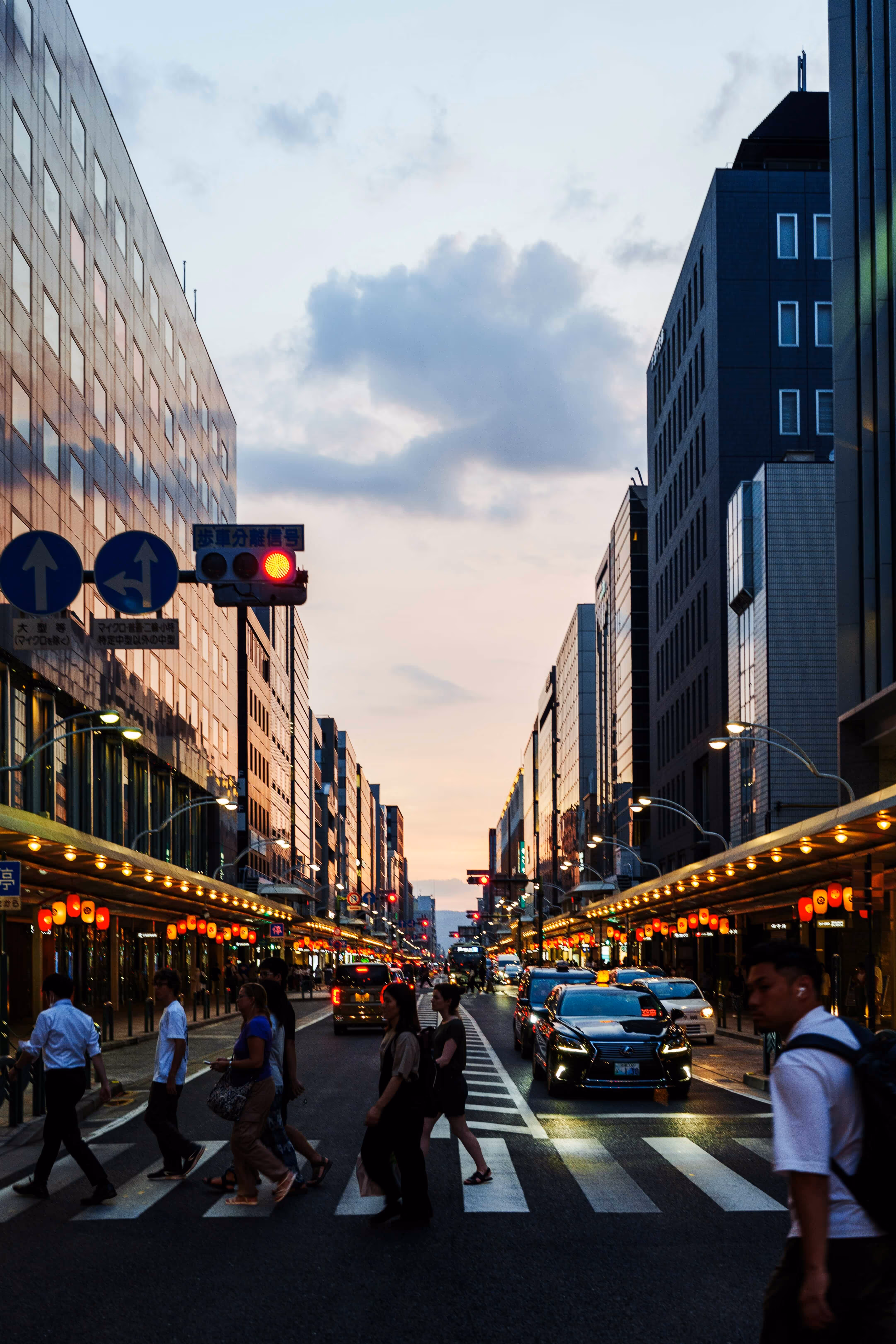 A photo of a busy city street in Kyoto. Many people are walking on the crosswalk.