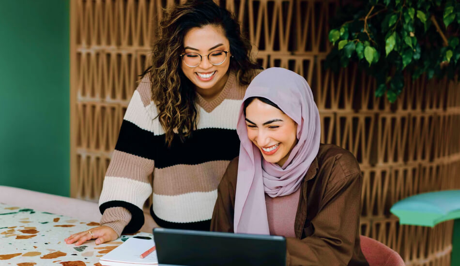 Two Women Sitting At a Table With a Laptop