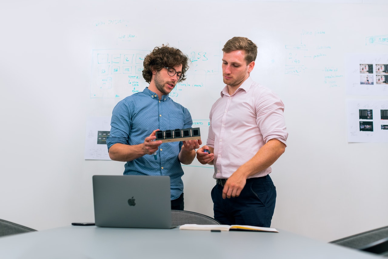 two people in front of a whiteboard looking at and discussing a prototype