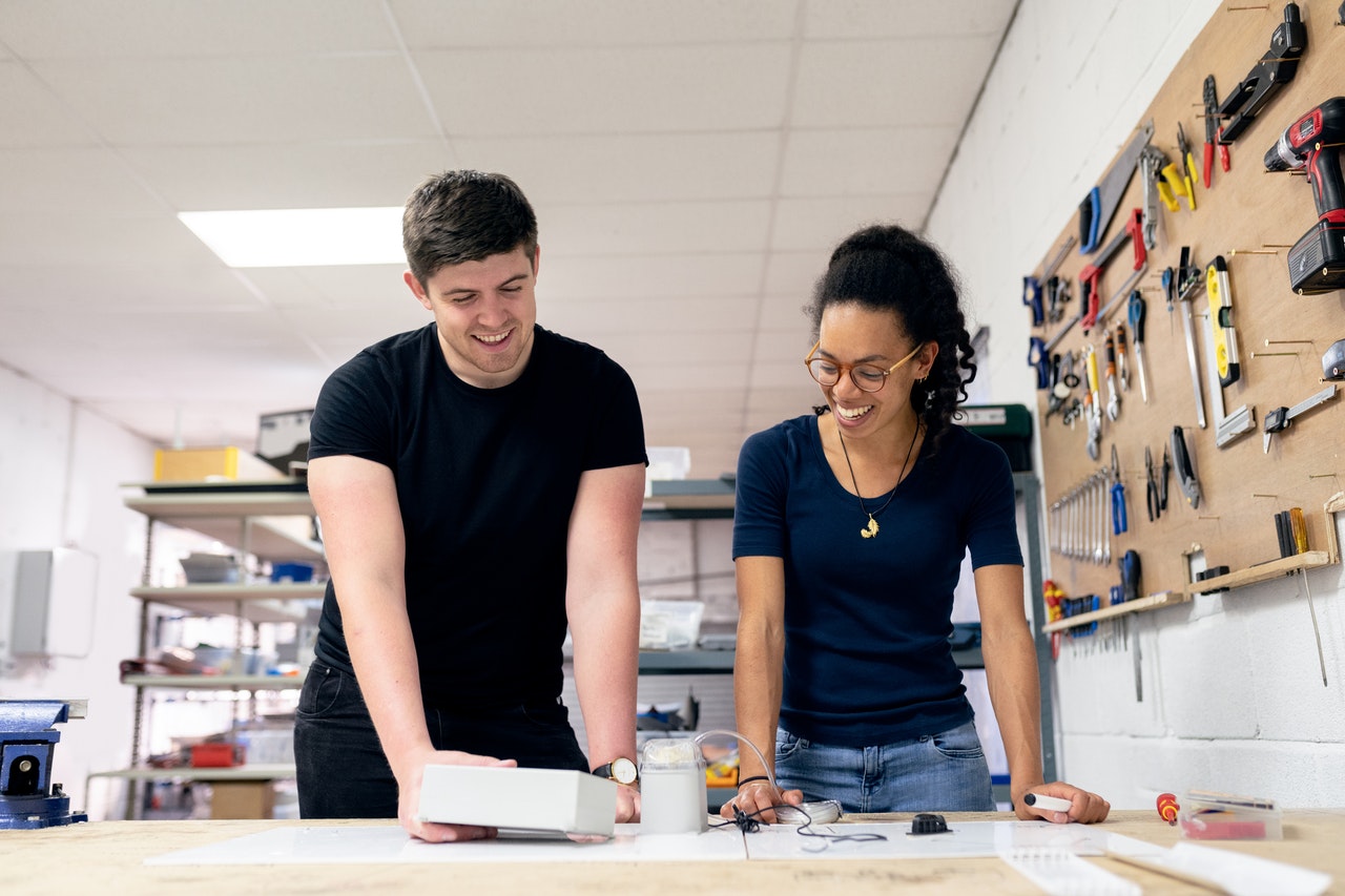 two people smiling as they stand over a shop table looking at a prototype