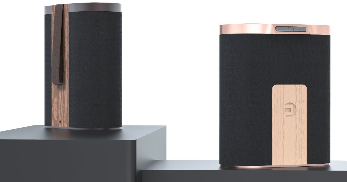 Two black cylindrical electronic devices on gray display blocks, one with a copper side panel and a small button.
