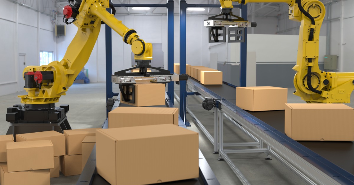 Two yellow robotic arms moving cardboard boxes along conveyor belts inside a bright industrial workspace.