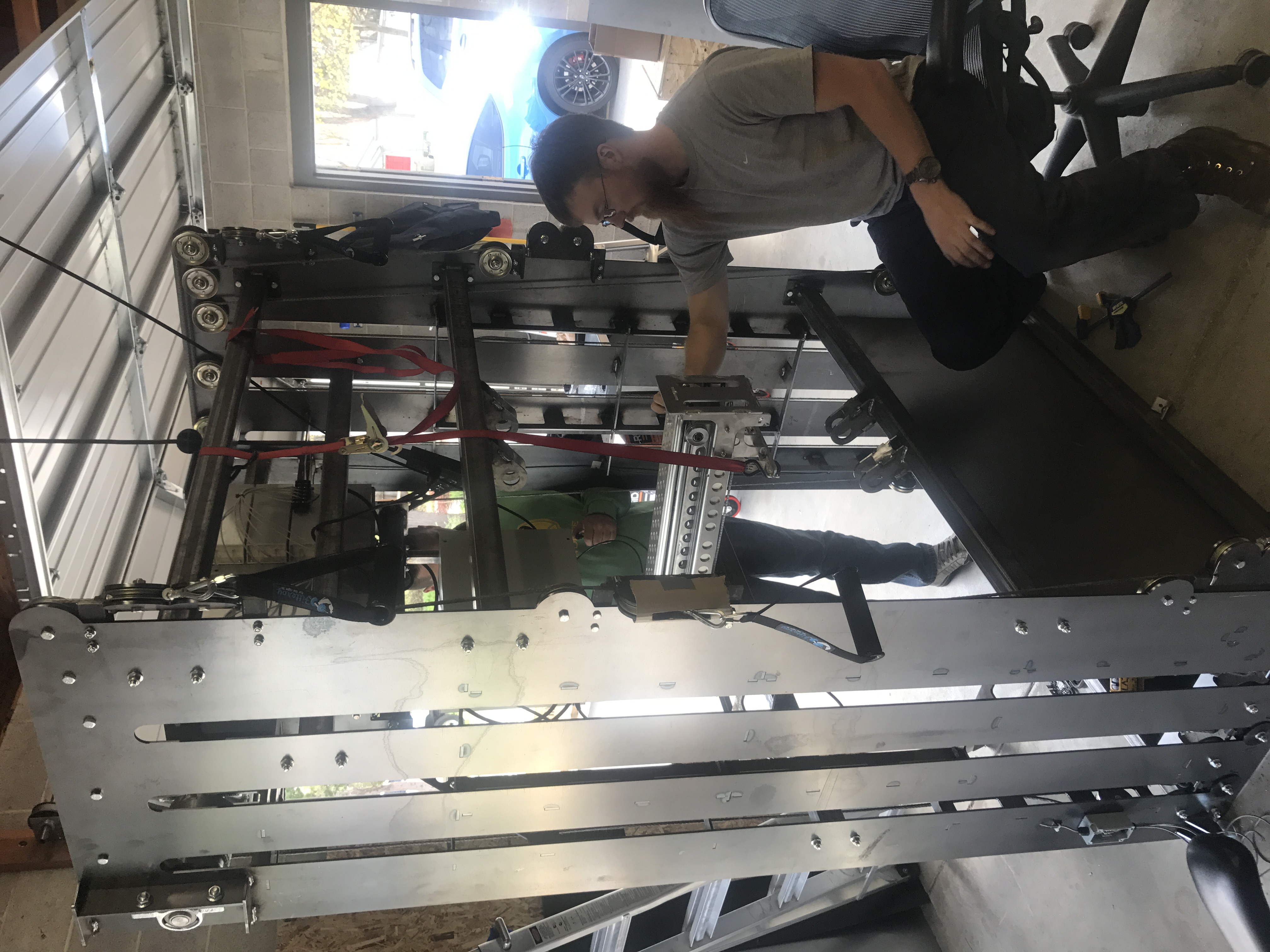 Engineer adjusts a large metal motion platform in a garage workshop while another person assists behind.