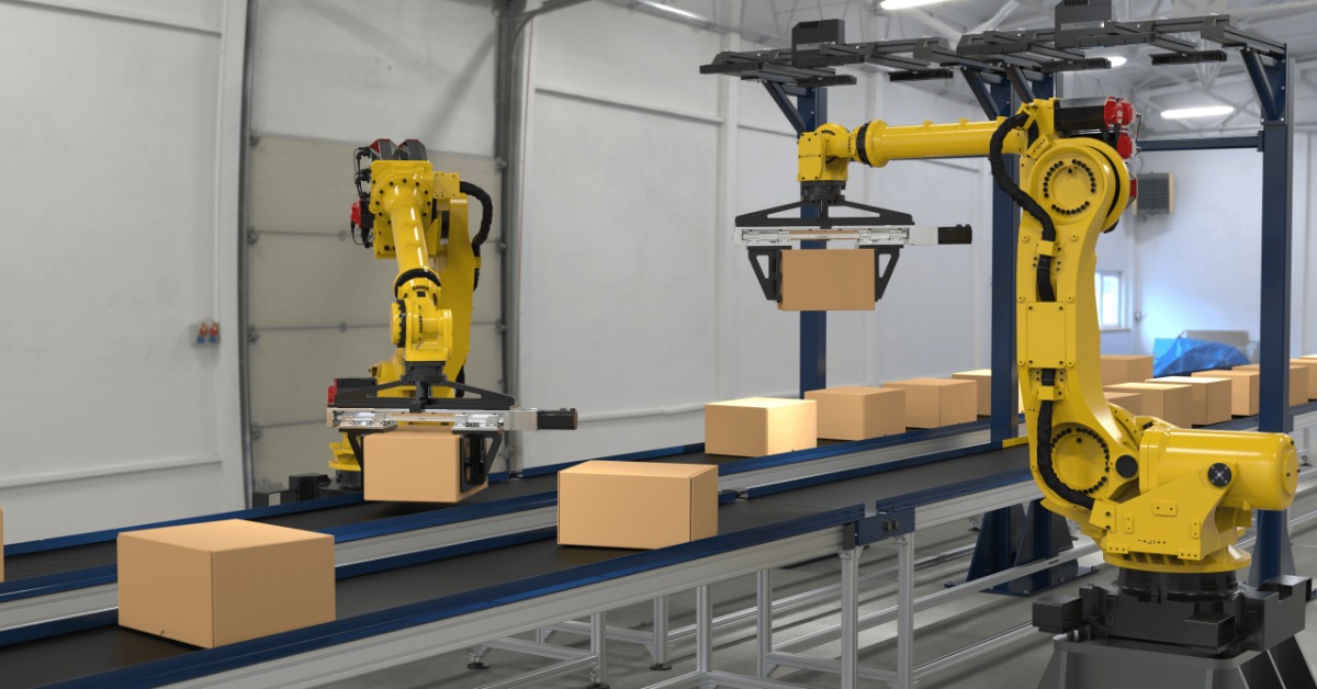 Two yellow robotic arms move cardboard boxes along parallel conveyor belts inside an automated facility.