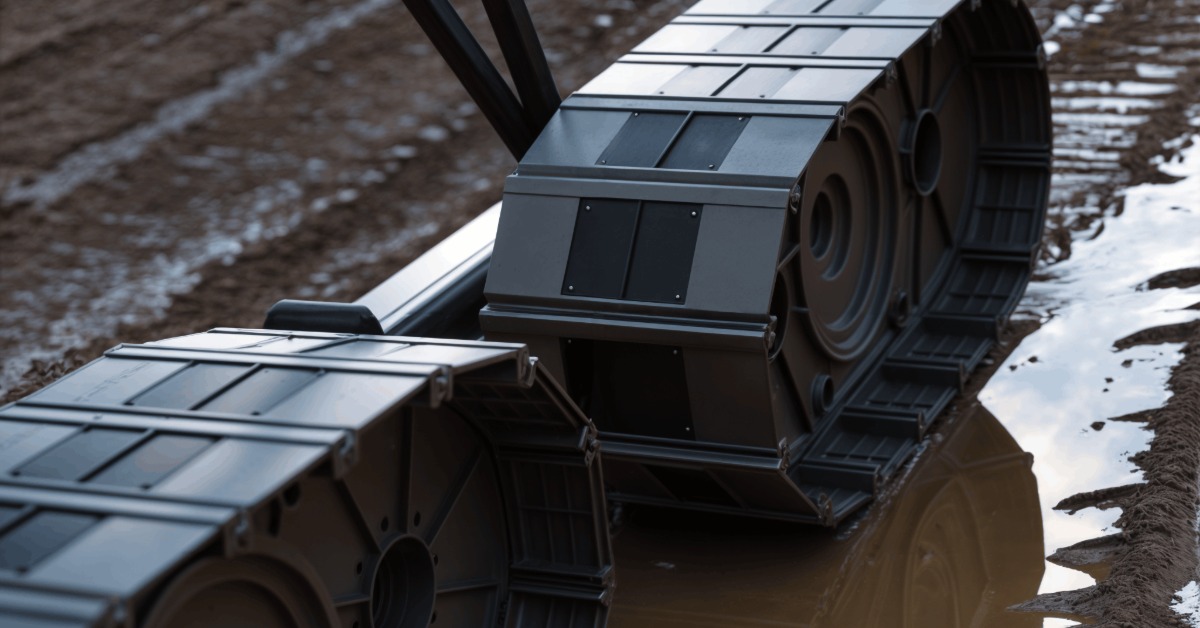 Heavy-duty black industrial cable chains with linked protective covers resting in a muddy trench filled with water.