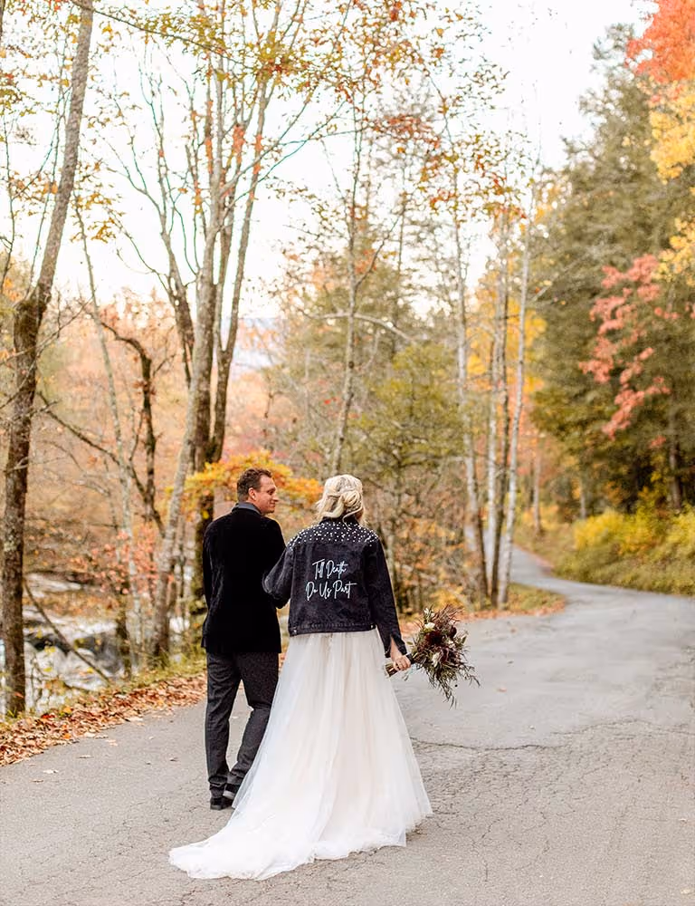An eloped couple walking down the street by a creek in the Smokies.