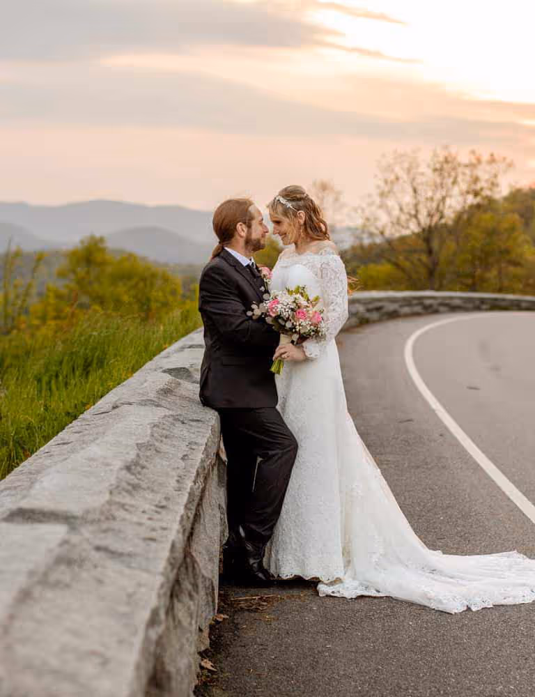 A couple posing for a photo with Let's Elope in Foothills Parkway with mountains and sunset in the background
