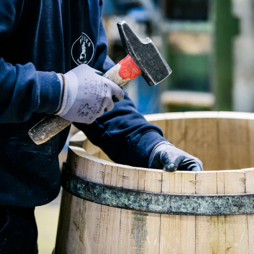 Cooper hammering a wooden wine barrel during its assembly.