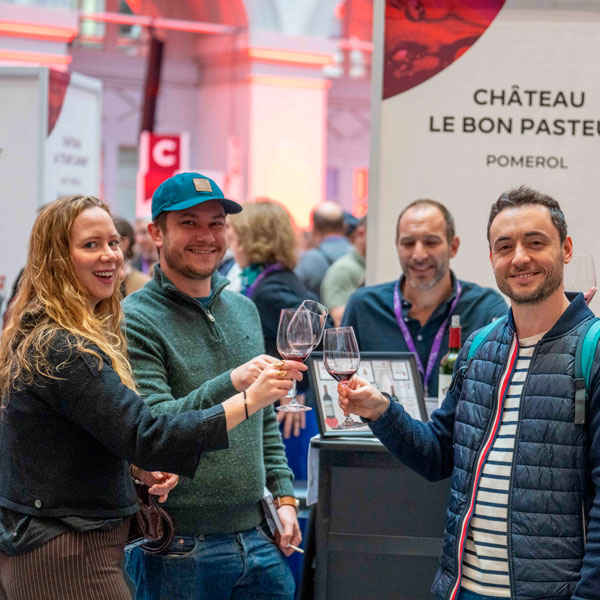 Visitantes disfrutando de una cata de vinos en un stand de productores durante Bordeaux Tasting 2025, compartiendo un momento distendido alrededor de copas de vino.