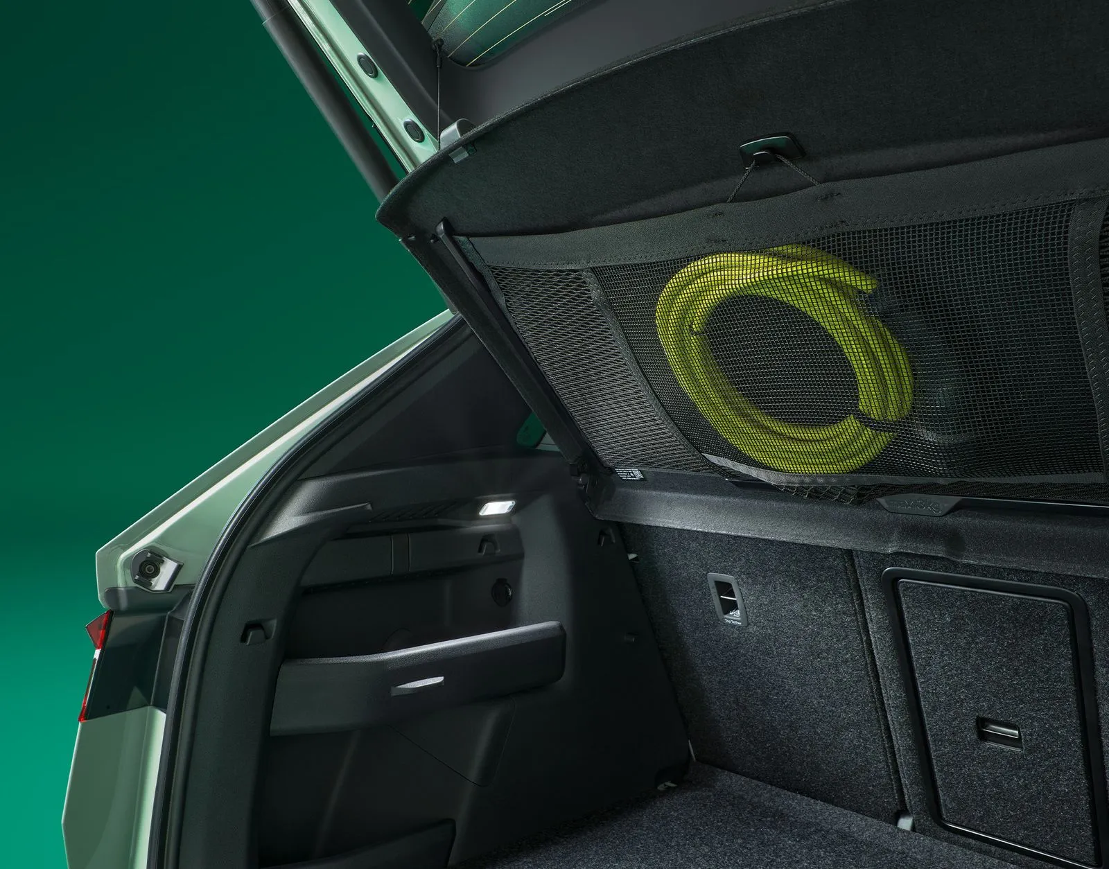 Detailaufnahme des geöffneten Kofferraums des Škoda Elroq. In einem Aufbewahrungsnetz auf der Unterseite der Heckablage ist ein Ladekabel in hellgrüner Neonfarbe verstaut.