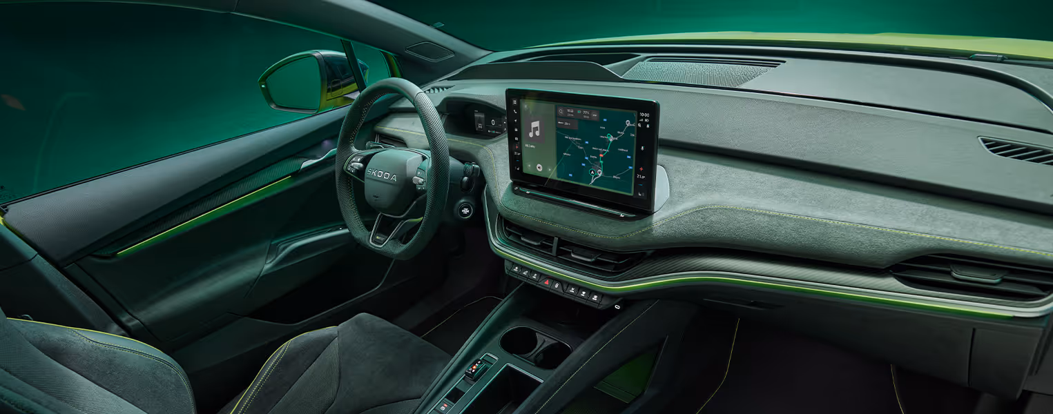 Innenraum des Škoda Elroq RS mit Blick auf das Lenkrad und den freistehenden 13-Zoll-Infotainmentbildschirm. Das Interieur ist mit schwarzem Kunstleder und Suedia Microfaser sowie grünen Ziernähten und Carbon-Dekorleisten gestaltet.