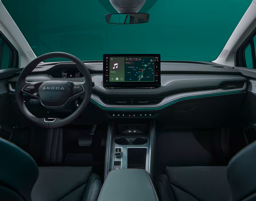Blick über die Mittelarmlehne auf das Lenkrad, das Infotainmentsystem und das Armaturenbrett im Škoda Elroq. Türkise Ambient-Beleuchtung.