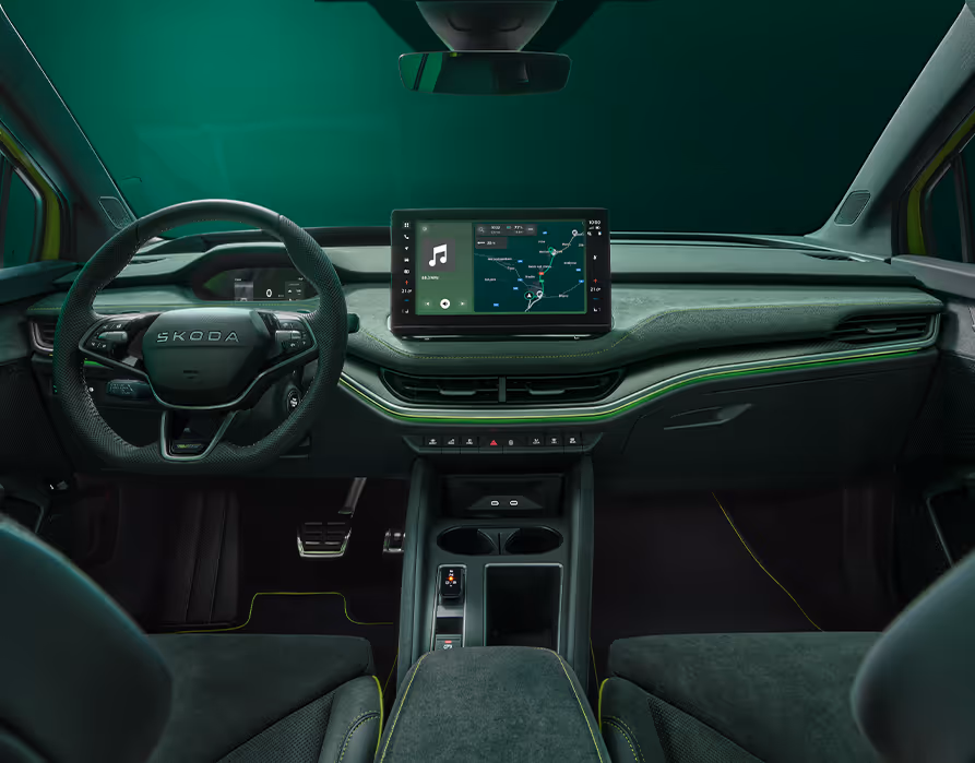 Blick über die Mittelarmlehne auf das Lenkrad, das Infotainmentsystem und das Armaturenbrett im Škoda Elroq RS. Grüne Ambient-Beleuchtung.