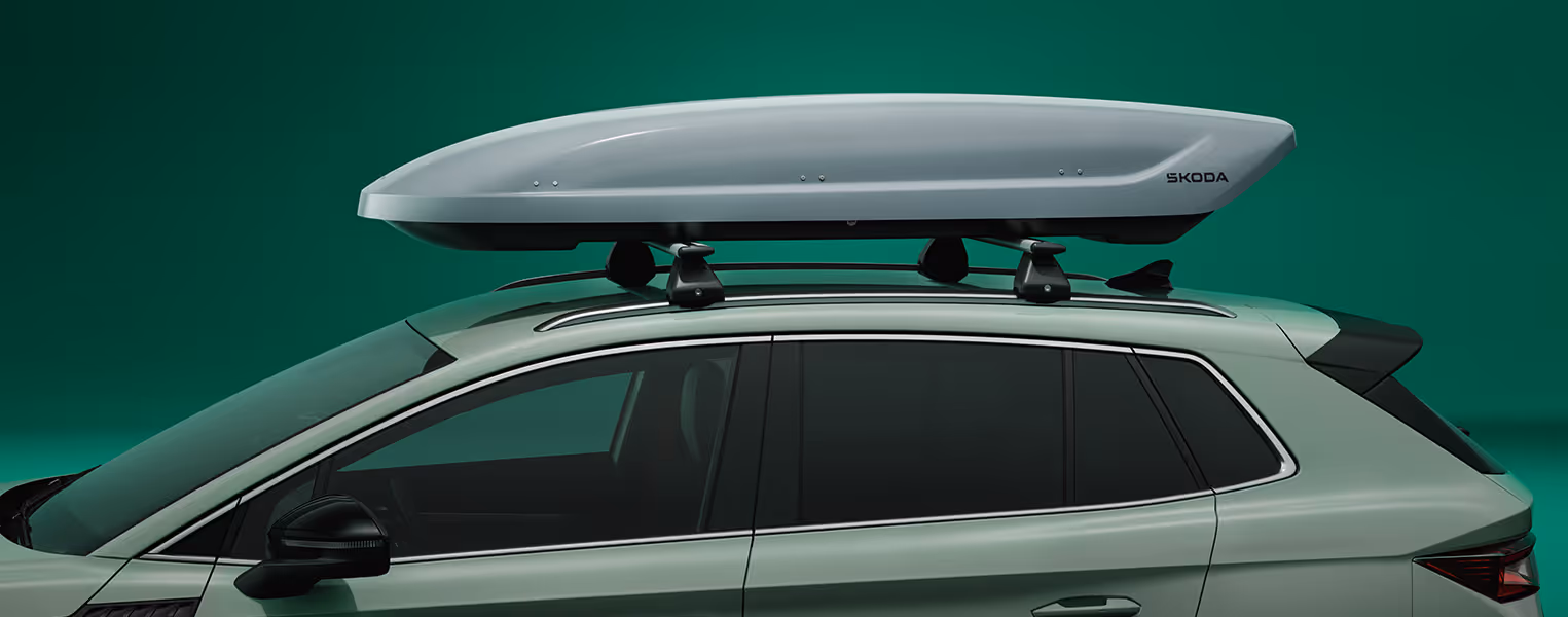 Nahaufnahme einer schwarzen Dachbox mit Škoda-Logo, die auf dem Dach eines Škoda Elroq montiert ist. Die Box und die Befestigungselemente können durch ein Plus-Zeichen gesondert angewählt werden.