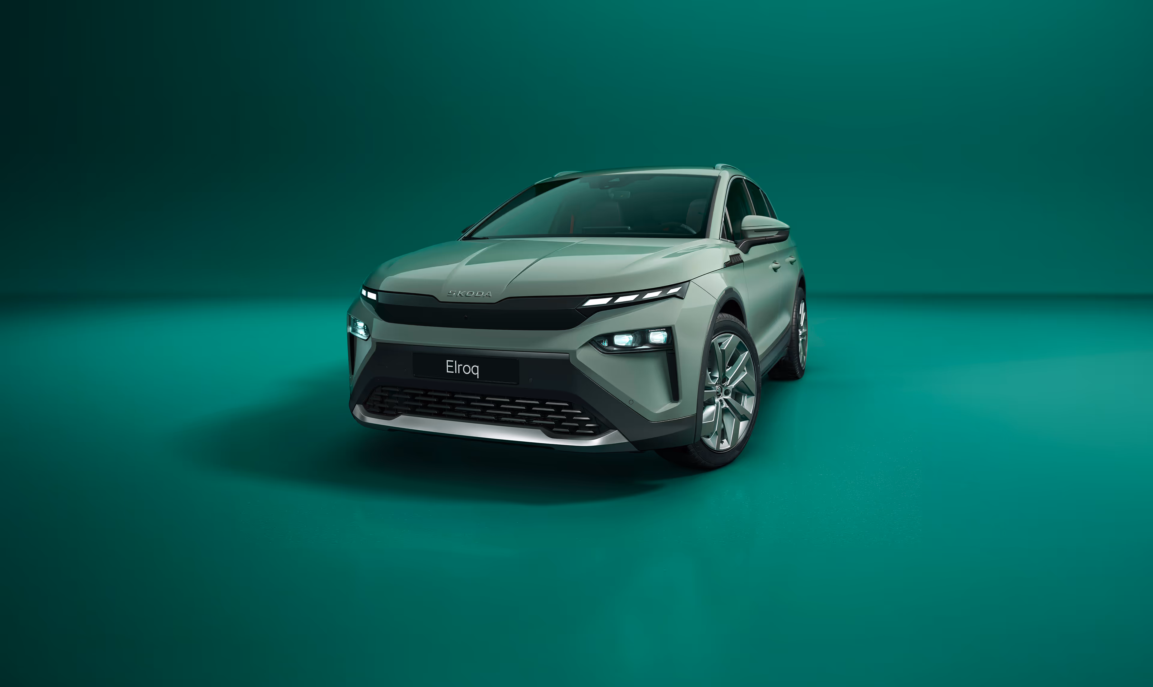 Frontalansicht des Škoda Elroq in der Farbe Timiano-Grün vor einem grünen Studiohintergrund. Die LED-Matrix-Scheinwerfer des Fahrzeugs leuchten und betonen das moderne Design der Frontpartie.