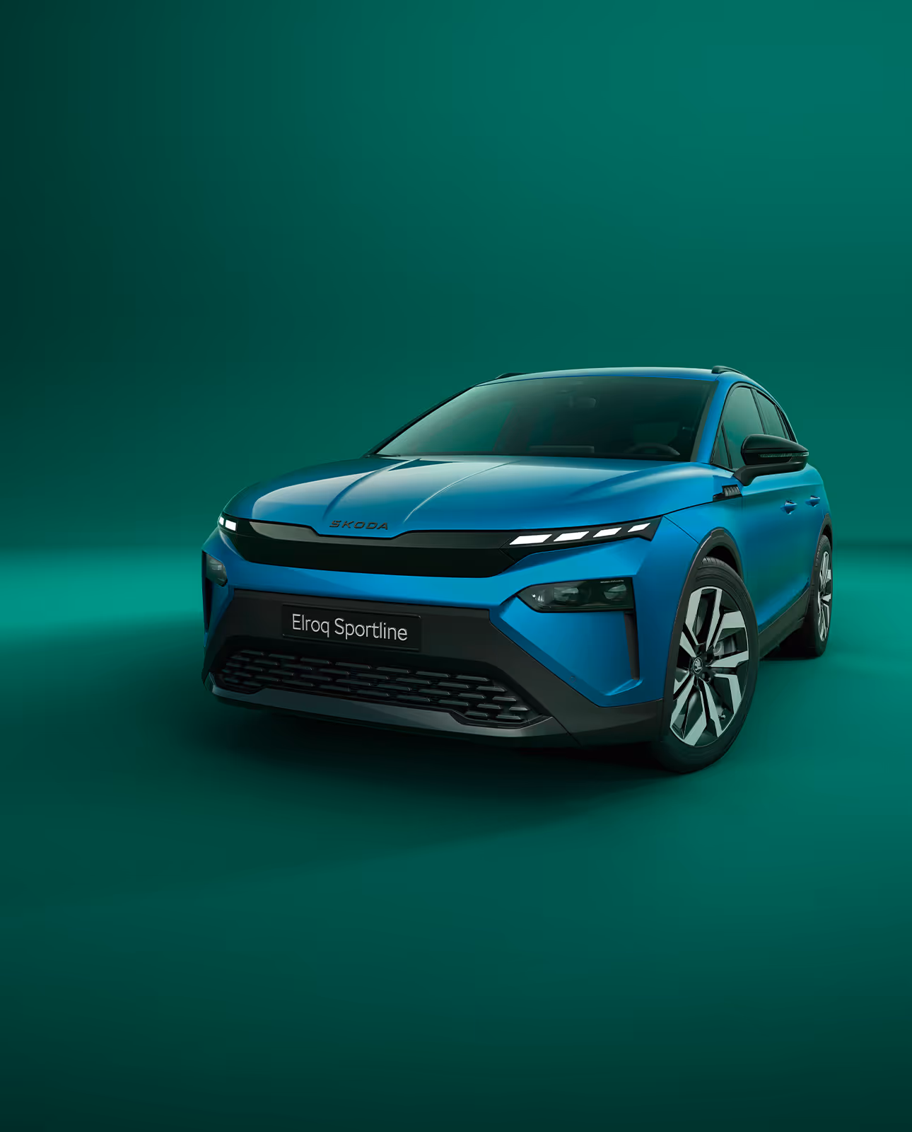 Frontalansicht des Škoda Elroq Sportline in der Farbe Race-Blau Metallic vor grünem Studiohintergrund. Das Fahrzeug zeichnet sich durch schwarze Designelemente am Kühlergrill und an der Frontschürze aus.