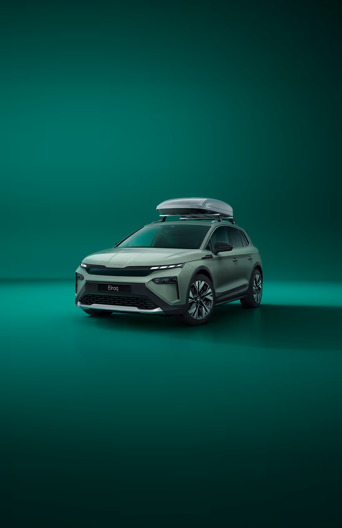 Frontalansicht eines Škoda Elroq mit einer Dachbox vor grünem Studiohintergrund. Das Fahrzeug ist für eine Reise mit zusätzlichem Gepäck ausgestattet.