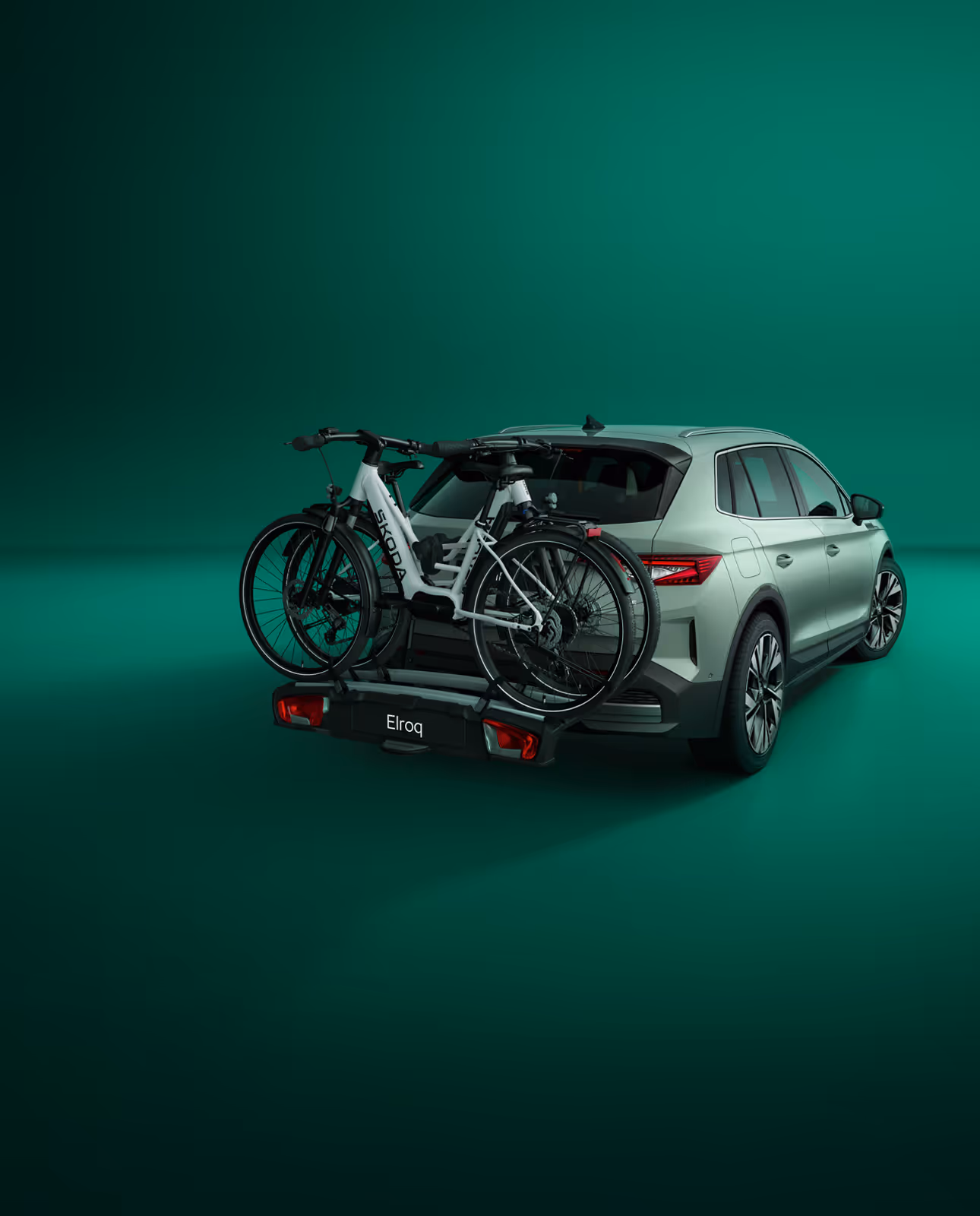 Heckansicht eines Škoda Elroq mit einem Fahrradträger auf der Anhängerkupplung vor grünem Studiohintergrund. Auf dem Träger sind zwei Fahrräder mit Škoda Schriftzug auf dem Rahmen montiert.