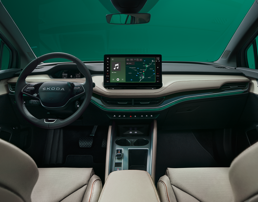 Eine symmetrische Weitwinkelaufnahme zeigt das Cockpit des Škoda Elroq aus der Perspektive der Rücksitze. Das elegante Interieur der Design Selection „L&K“ besticht durch beige Lederbezüge mit cognacfarbenen Ziernähten, akzentuiert durch eine grüne Ambientebeleuchtung.