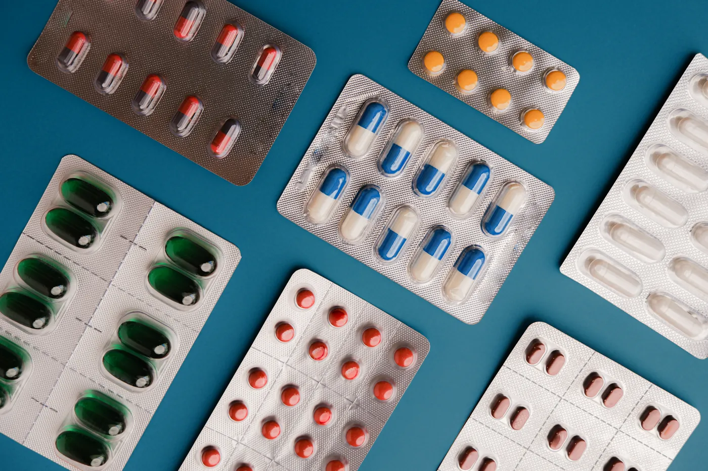 Medication capsules and blister packs on a deep teal background