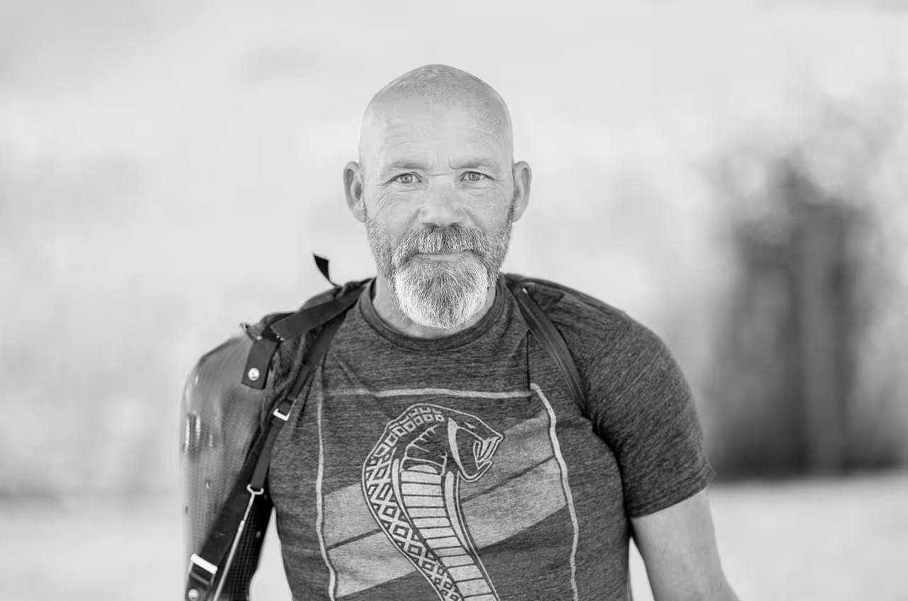 Bald man with beard smiling, wearing cobra shirt and shoulder bag