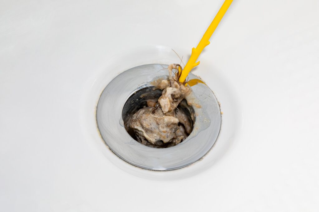 Cleaning hair and soap scum from clogged shower and bathtub drain. Plumbing repair, home maintenance and hair loss concept.