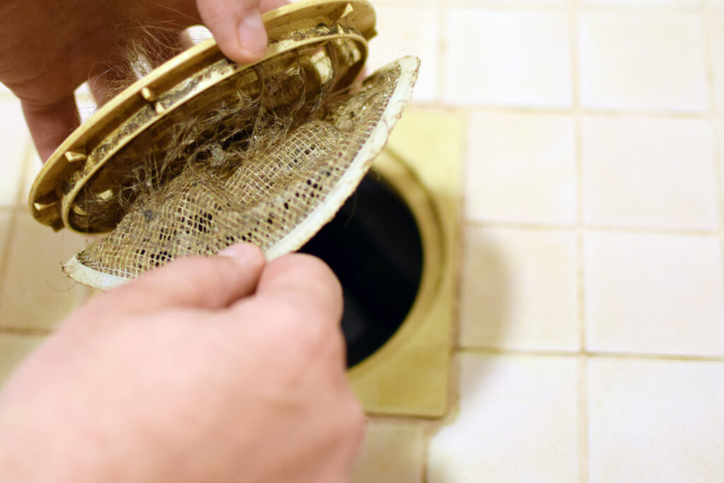 Removing filthy hair catcher filter net from shower drain. Copy space.