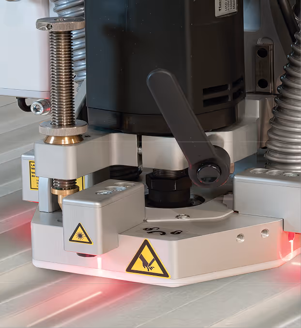 Close-up of a precision industrial machine component with adjustment screws, warning labels, and red laser guides.