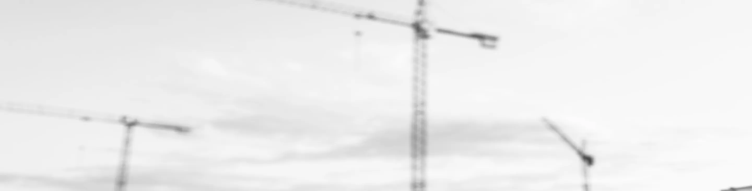 Three construction cranes against a cloudy sky.