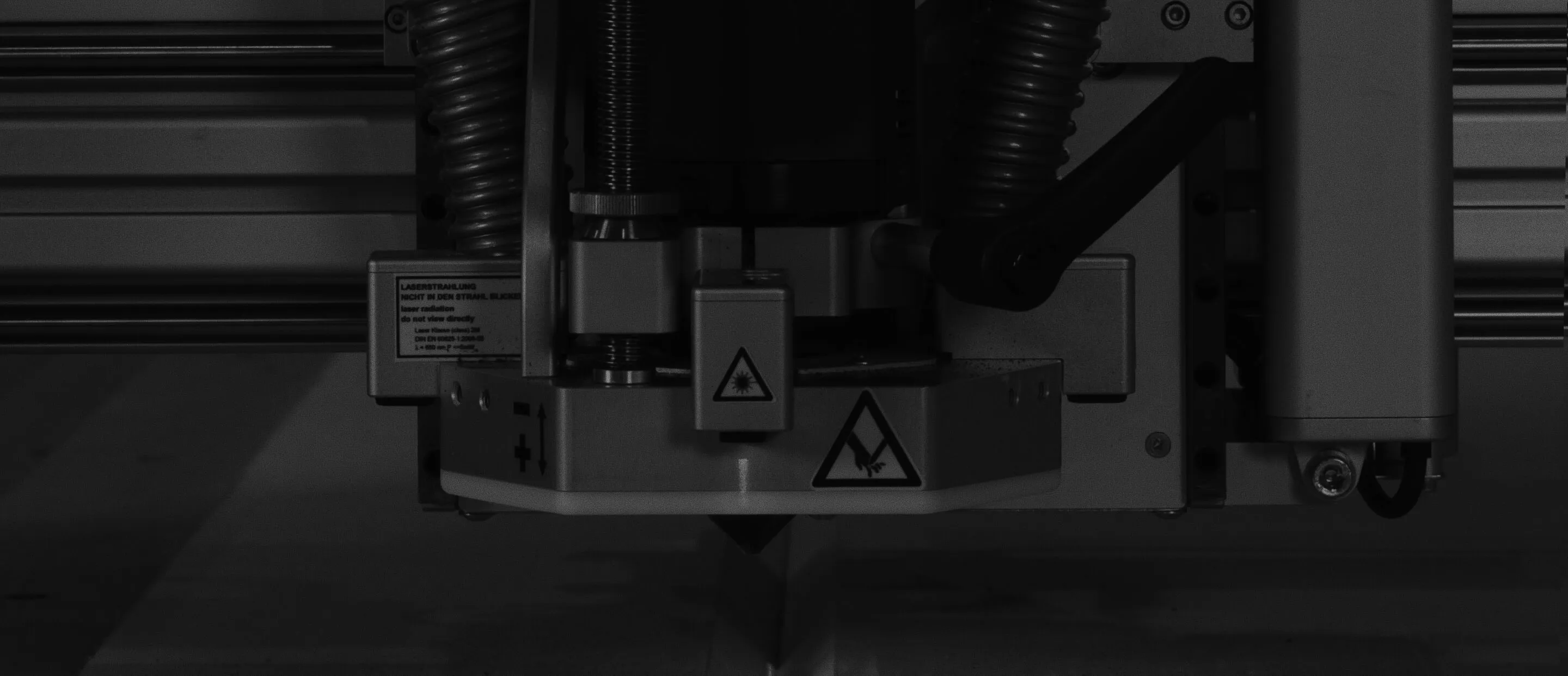 Close-up of an industrial laser cutting machine head with warning labels.