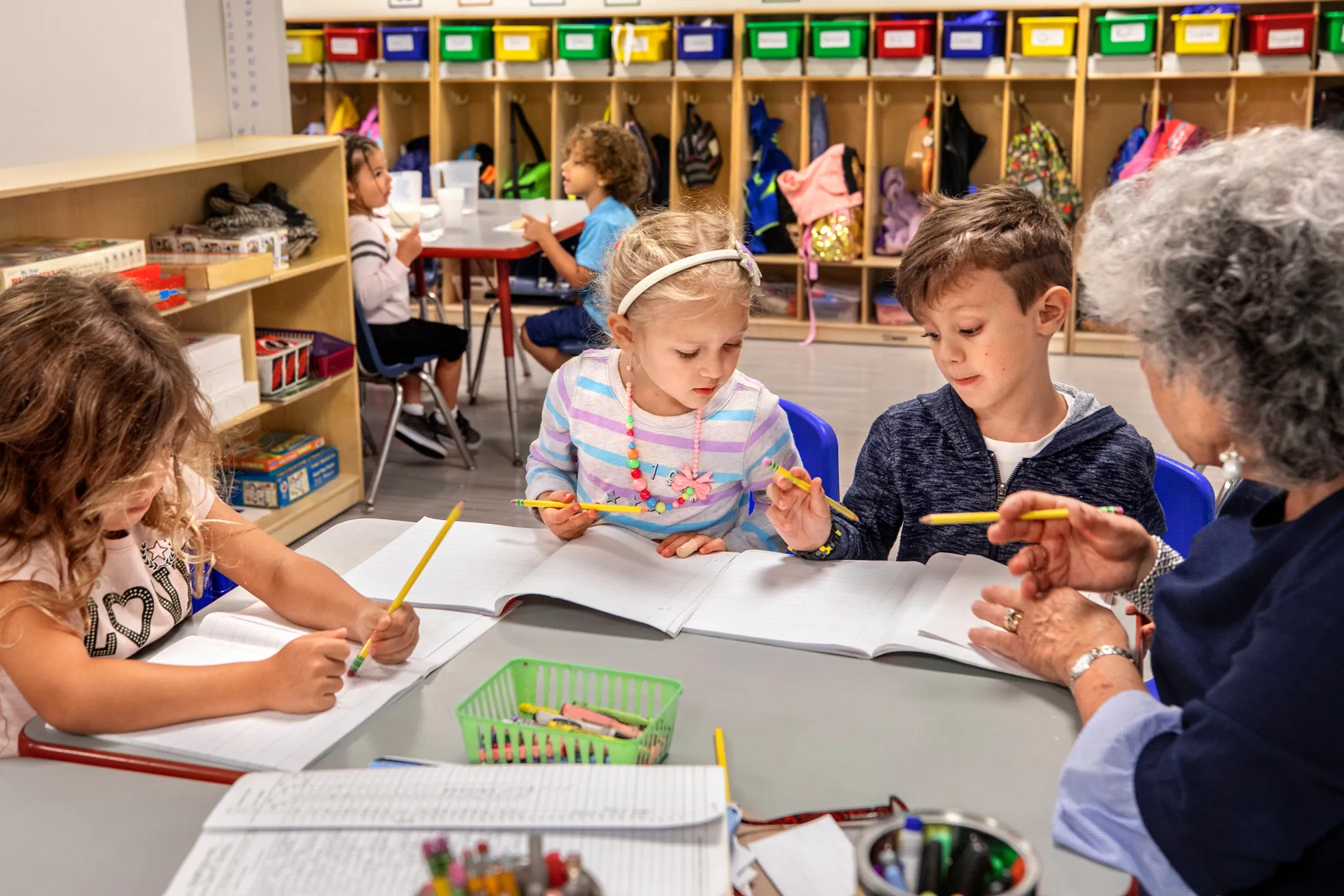 A group of elementary school kids around a table, coloring with their teacher.