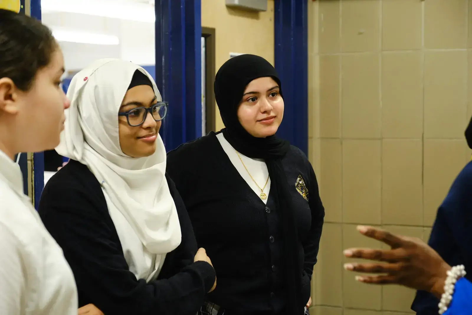 Three students in school uniforms listening attentively to a speaker
