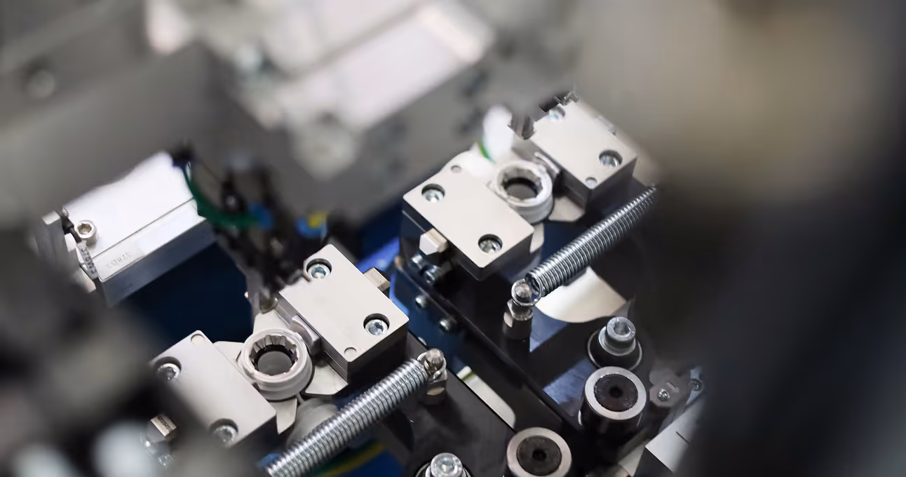 Close-up of mechanical assembly equipment with metal parts and screws in a manufacturing setting.