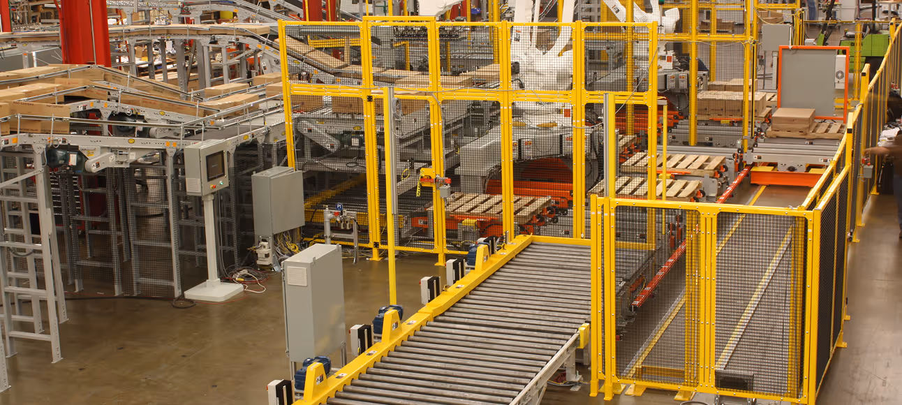 Automated industrial conveyor system with yellow safety fencing in a factory setting.