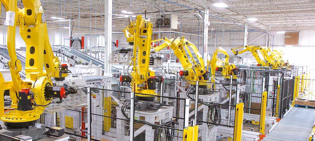 Row of yellow industrial robotic arms operating in a modern manufacturing facility.