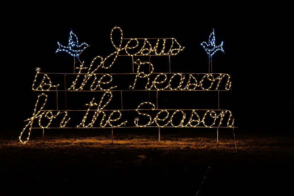 Greenville, NC Christmas light display at night with the message 'Jesus is the Reason for the Season' in yellow lights, featuring two blue light doves on each side.