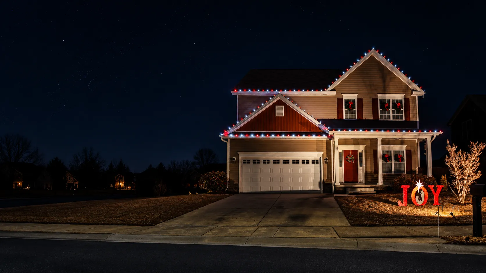 A two-story house in Ayden, NC decorated with red and white Christmas lights along the roof edges, wreaths with red bows on the front door and windows, and a brightly lit yard sign spelling JOY with a star and nativity scene silhouette inside the O, under a starry night sky all installed by Walston Evans Home Services