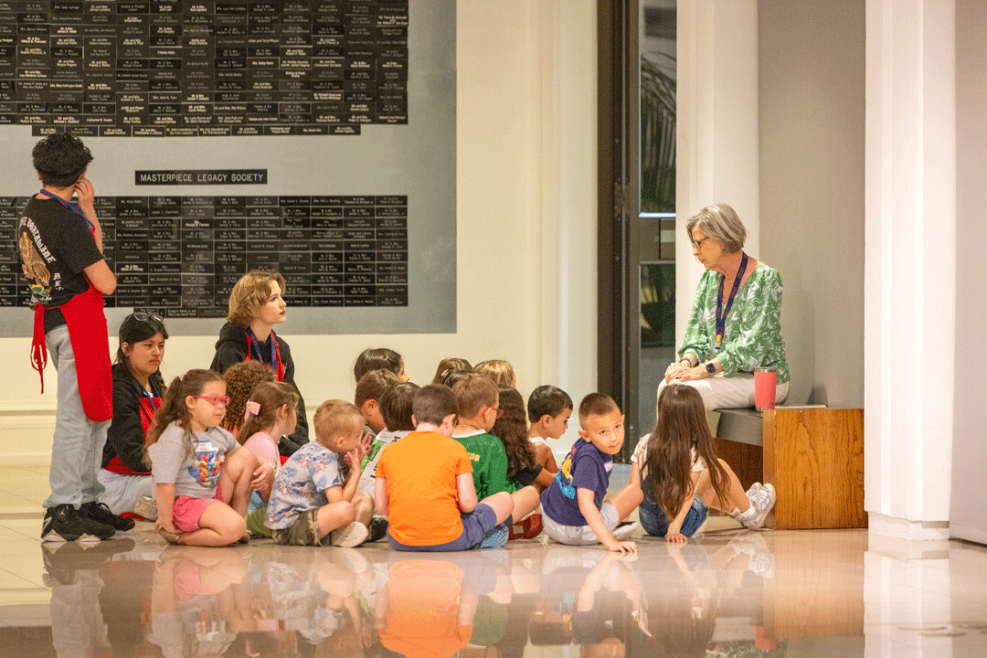 school children sitting on the floor in front of art listening to an instructor