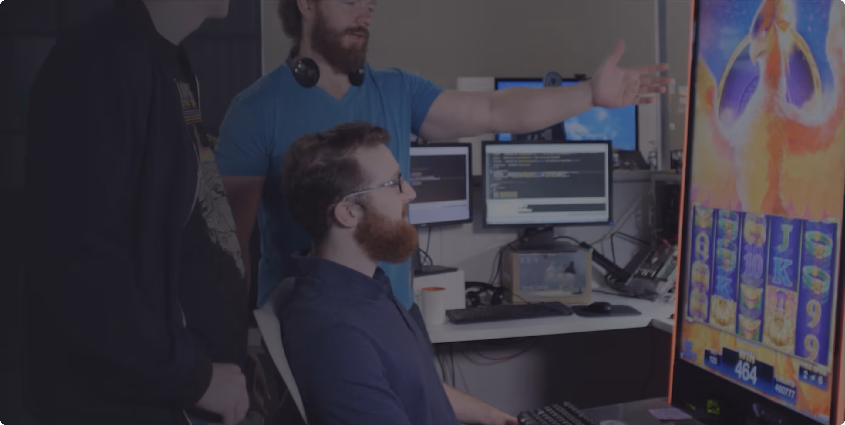 AGS developers discussing code with game screen and multiple monitors