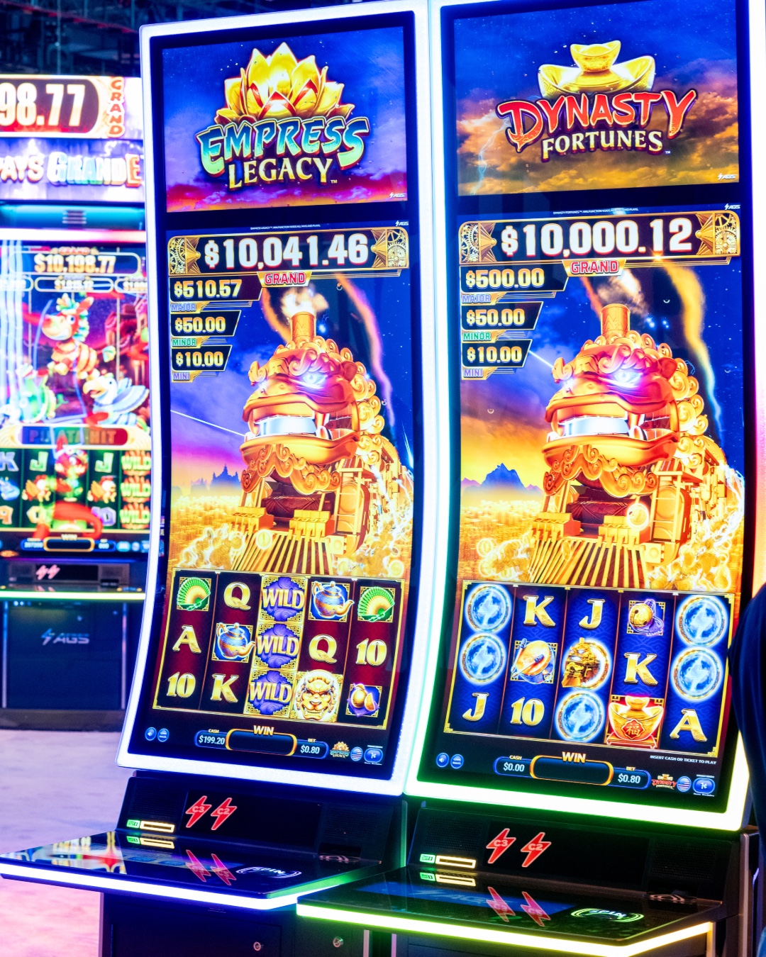A woman holding a microphone stands next to a brightly lit slot machine featuring a werewolf design at a gaming convention.